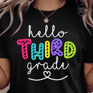 May include: A black t-shirt featuring the white cursive text hello and grade with a small heart icon. The word THIRD is printed in large, colorful, block letters with a diagonal striped pattern in shades of pink, teal, yellow, purple, and lime green.