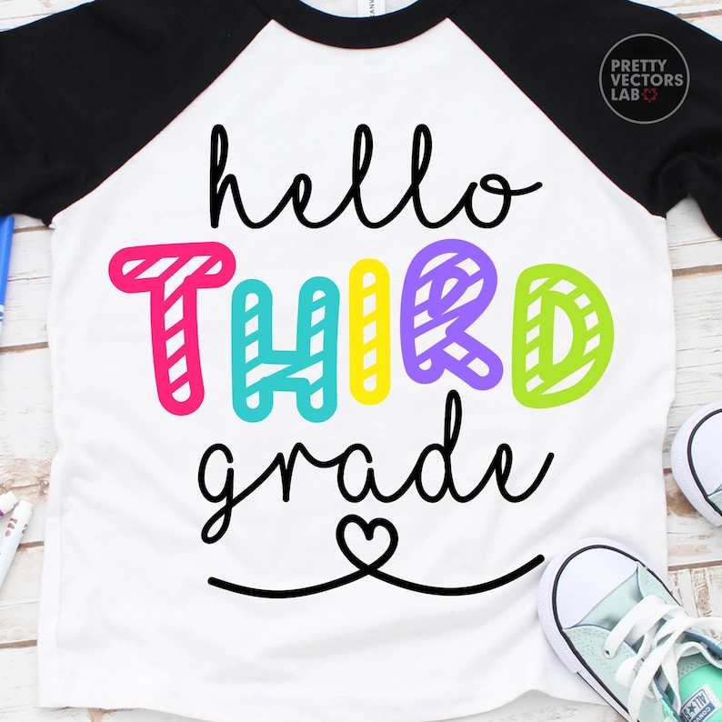 May include: A white raglan t-shirt with black sleeves featuring the black cursive text hello, the colorful striped block text THIRD, and the black cursive text grade with a heart icon below. The design includes pink, teal, yellow, purple, and lime.