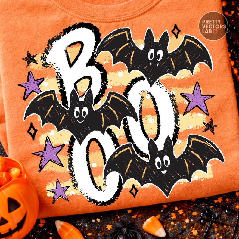 May include: An orange t-shirt featuring a graphic print with the word BOO in large white letters with black distressed outlines. Three black cartoon bats with white eyes and fangs are positioned around the letters, accented by purple stars.
