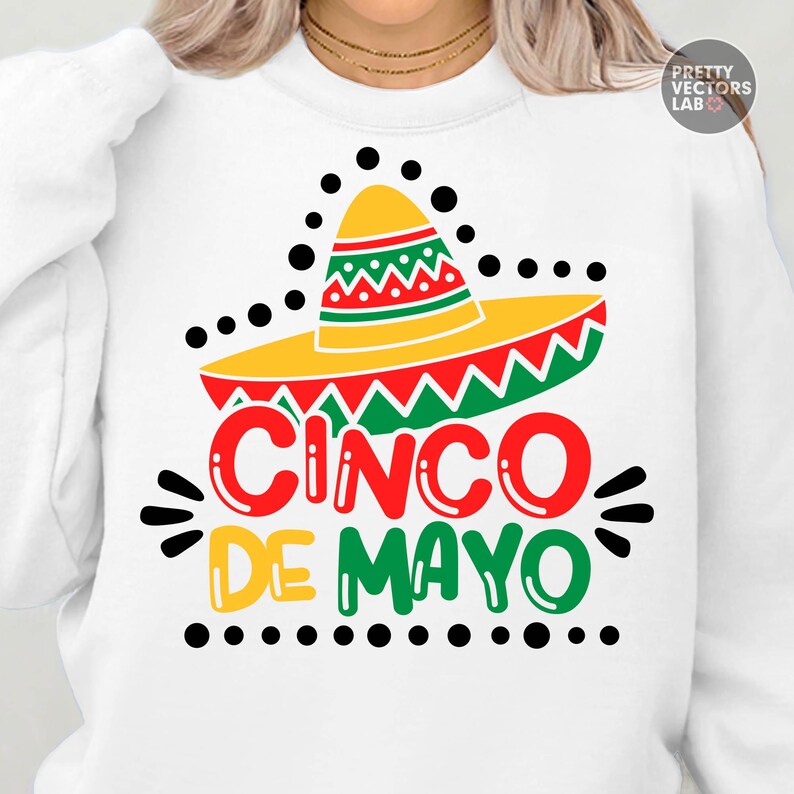 K&ouml;nnte beinhalten: Wei&szlig;es Sweatshirt mit einem farbenfrohen Cinco de Mayo-Design. Die Grafik zeigt einen gelben Sombrero mit roten, gr&uuml;nen und gelben Akzenten und die Worte "Cinco de Mayo" in Rot, Gelb und Gr&uuml;n.