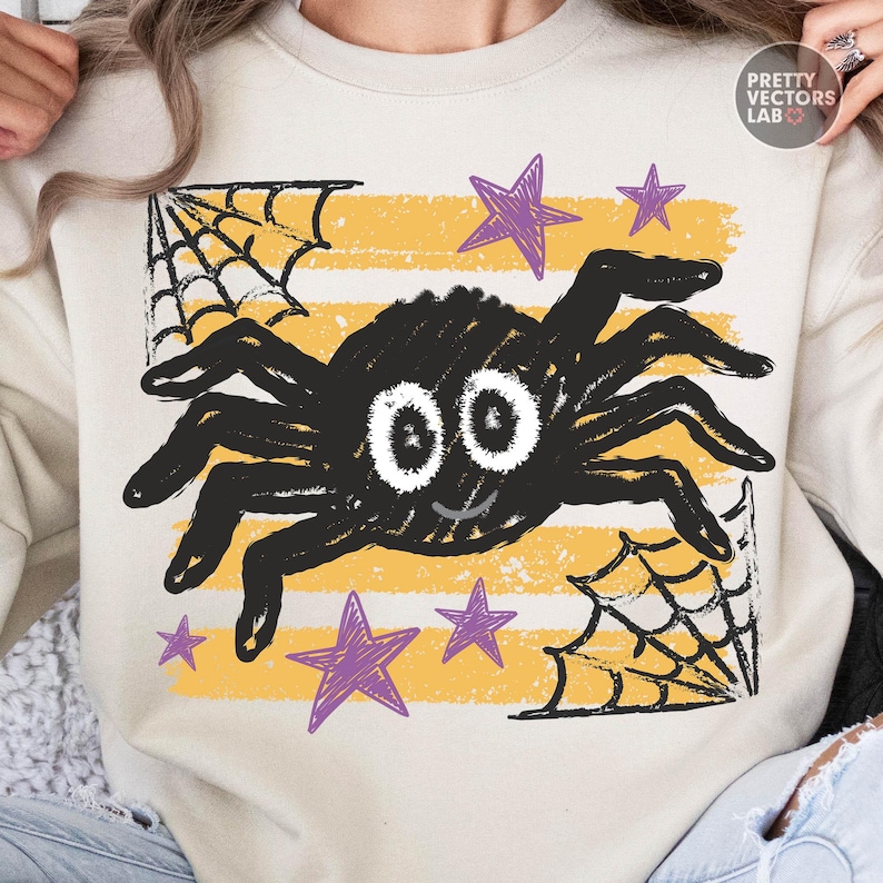 May include: A beige crewneck sweatshirt featuring a graphic of a black spider with large white eyes, surrounded by purple stars and black spiderwebs over horizontal yellow stripes. The text PRETTY VECTORS LAB is printed in the upper right corner.