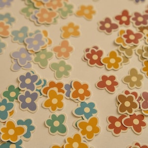 Puede incluir: Una colección de pegatinas de flores de colores en varios tonos de azul, verde, amarillo, naranja y rojo. Las pegatinas están dispuestas en un patrón aleatorio sobre un fondo blanco.