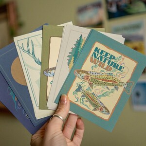 May include: A set of five cards with nature-themed illustrations. The cards are blue, green, and beige with illustrations of fish, trees, and a deer. The text on one card reads "Keep Nature Wild".