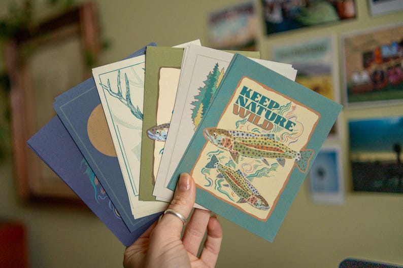 May include: A set of five cards with nature-themed illustrations. The cards are blue, green, and beige with illustrations of fish, trees, and a deer. The text on one card reads "Keep Nature Wild".