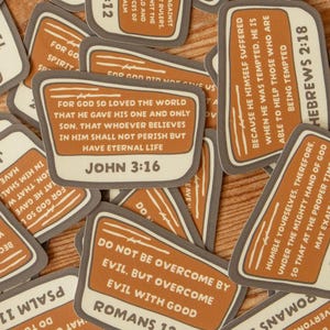 Peut inclure: Une collection d'autocollants rectangulaires aux coins arrondis, avec un fond orange brûlé et des bordures gris foncé. Chaque autocollant affiche un verset biblique unique en texte blanc, incluant des références comme Jean 3:16, Romains 12:21 et Hébreux 2:18.
