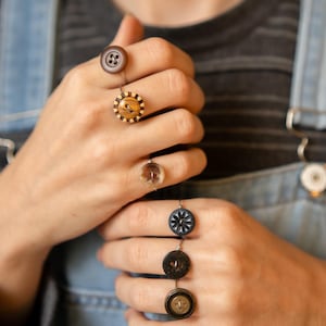 May include: Five rings with different buttons attached. The buttons are made of wood, plastic, and metal. The rings are silver in color.