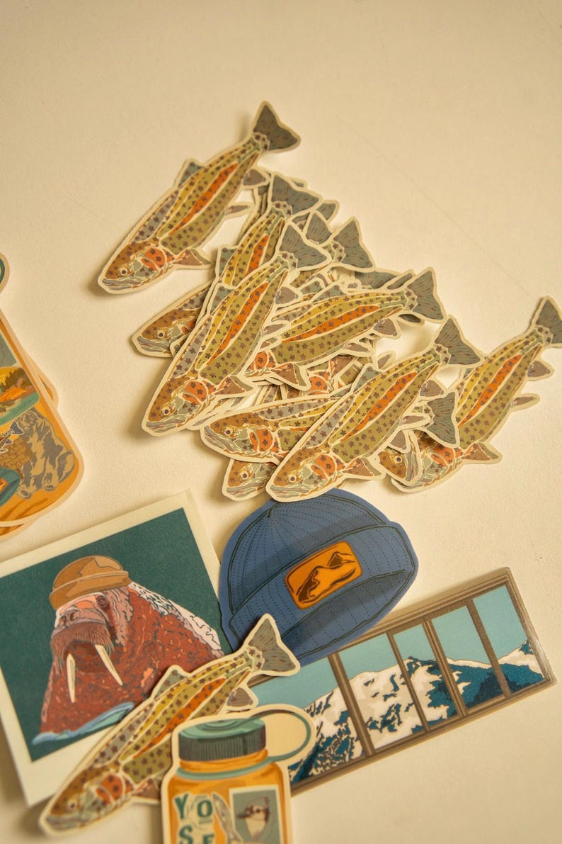 May include: A collection of colorful stickers featuring a variety of designs, including a walrus, a mountain scene, a blue beanie with a mountain logo, and a series of trout fish. The stickers are perfect for adding a touch of nature to your belongings.