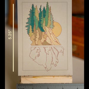 May include: A print of a forest scene with a sun setting behind a mountain range. The print is on a beige background and measures 3.75 inches wide by 5.25 inches tall.
