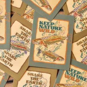 May include: A collection of rectangular greeting cards featuring a graphic illustration of two trout swimming in water. The cards display the text KEEP NATURE WILD or SHARE THE EARTH in bold lettering, with the fish decorated in colorful star patterns.