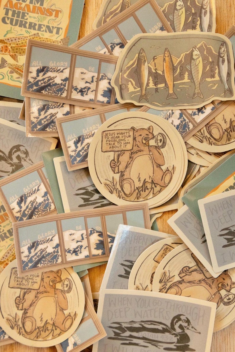 Op de afbeelding: Een verzameling stickers met diverse ontwerpen en tekst. Sommige stickers tonen berglandschappen, vissen en een beer met een bord met de tekst "JESUS WANTS TO HEAR YOUR PROBLEMS TALK TO HIM ABOUT IT". Andere stickers hebben zinnen als "ALL GLORY BE".