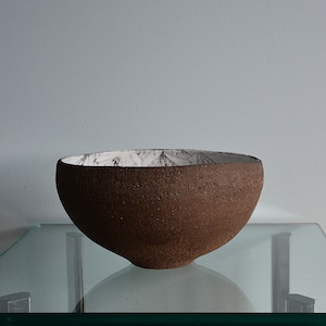 May include: A brown ceramic bowl with a white interior. The bowl has a rough, textured exterior and a smooth, white interior.