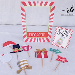 May include: A collection of Christmas-themed photo booth props. Includes a red and white striped frame with "ELFIE SELFIE" text, signs that say "LET'S TAKE AN ELFIE!", "NAUGHTY", and "NICE", and various cutouts like a Santa hat and gift box.