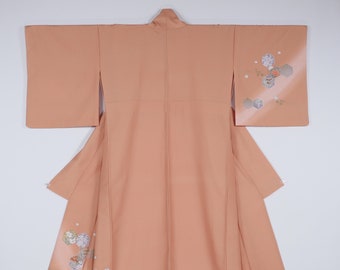 Könnte beinhalten: Ein pfirsichfarbener Kimono mit einem Blumenmuster. Der Kimono hat ein traditionelles japanisches Design mit einem breiten Kragen und langen Ärmeln. Das Blumenmuster ist in Weiß-, Rosa- und Grüntönen gehalten.
