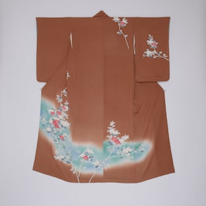 May include: A brown silk kimono with a white and pink floral pattern. The flowers are arranged in a flowing design on the lower half of the kimono.