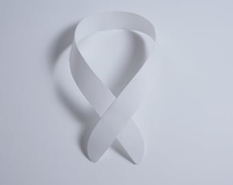 May include: A white ribbon tied in a loop, creating a figure eight shape. The ribbon is made of a smooth, matte material and is lying flat on a white background.