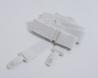 Puede incluir: Tirantes elásticos blancos con una hebilla y clips de plástico blanco. Los tirantes tienen un patrón sutil.