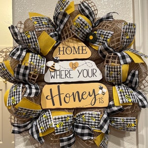 May include: A burlap wreath decorated with black and white checkered ribbon, yellow ribbon with a bee pattern, and a wooden sign that reads "Home is where your Honey is".