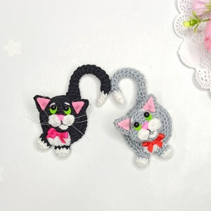May include: Two crocheted cat ornaments, one black and white with a pink bow, and one gray and white with a red bow.