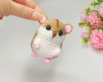 May include: A small crocheted hamster toy with brown and white fur, pink ears, and black eyes.