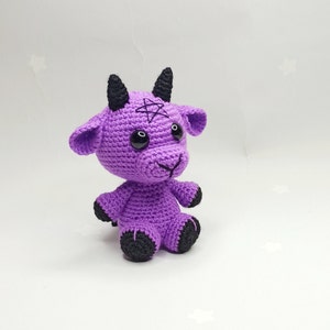 Peut inclure: Peluche de ch&egrave;vre en crochet violet avec des cornes, des yeux et des sabots noirs. La ch&egrave;vre a un pentagramme cousu sur son front.
