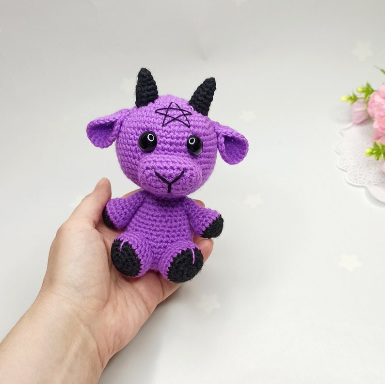 Peut inclure: Peluche de ch&egrave;vre en crochet violet avec des cornes, des yeux et des sabots noirs. La ch&egrave;vre a un pentagramme sur le front.