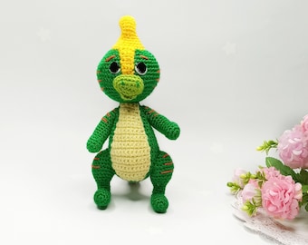 May include: A green and yellow crocheted dinosaur toy with orange accents. The dinosaur has a yellow crest and large black eyes.