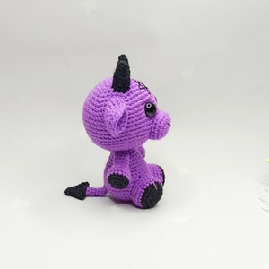 Peut inclure: Peluche en crochet violet en forme de diable avec des cornes noires, une queue et des yeux.