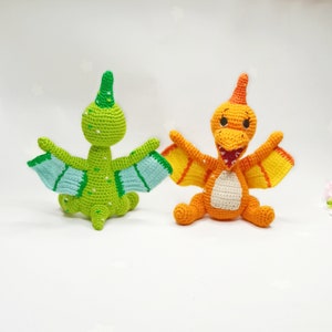 May include: Two crocheted dinosaur toys. One is green with light blue wings and the other is orange with yellow wings.