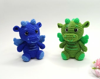 May include: Two crocheted dragon toys, one blue and one green, with wings and smiling faces.