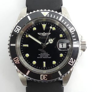 Op de afbeelding: Een zwart Invicta professioneel automatisch horloge met een roestvrijstalen bezel en een zwarte rubberen band. De wijzerplaat heeft lichtgevende markeringen en wijzers, en een datumweergave op 3 uur. Waterbestendig tot 200m.