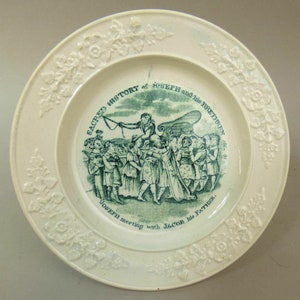 Peut inclure: Une assiette en céramique blanche avec une illustration verte détaillée représentant une scène biblique. L'assiette présente une bordure en relief floral et le texte "SACRED HISTORY at JOSEPH and his BRETHREN" et "Joseph meeting with JACOB his FATHER."