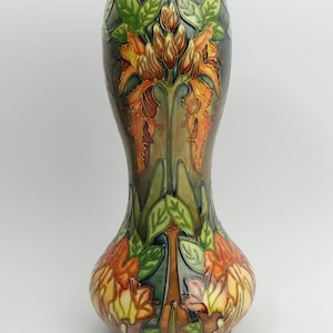 Puede incluir: Un jarrón de cerámica marrón alto, con base bulbosa y cuello estrecho. El jarrón está decorado con un patrón floral de flores naranjas, amarillas y verdes.