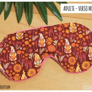 May include: A sleep mask featuring a dark red fabric with a repeating pattern of gnomes, orange flowers, and foliage. The mask has a pink minky fabric backing and a white elastic strap. Text on the image reads ADULTE - VERSO MINKY.