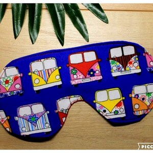 May include: A blue sleep mask decorated with a pattern of colourful camper vans. The vans feature floral and striped designs in pink, yellow, orange, and blue. The mask has a white elastic strap.
