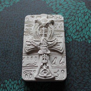K&ouml;nnte beinhalten: Wei&szlig;er Keramik-Ankh-Anh&auml;nger mit Hieroglyphen und einem gefl&uuml;gelten Skarab&auml;us-Design.