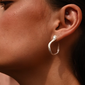 Könnte beinhalten: Silberne Schlangen-Creolen. Der Schlangenkopf befindet sich oben am Creolenring.