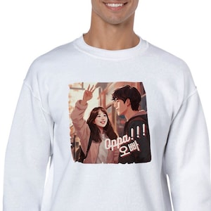 May include: White sweatshirt with a graphic print of a couple in a cartoon style. The graphic features a young woman waving to a young man with the text "Oppa!!" in Korean.