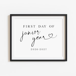 May include: A black framed sign featuring white background with black text that reads FIRST DAY OF junior year followed by a heart symbol and the date 2026-2027. The design uses a combination of bold sans-serif and elegant script typography.