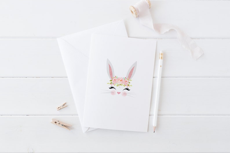 May include: A white bunny with pink eyes and a pink flower crown. The bunny is on a white card with a white background.
