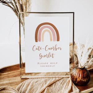 May include: A framed sign with a watercolor rainbow in shades of brown, pink, and beige. The sign reads "Cute-Cumber Gimlet" and "Please Help Yourself" in a stylish font. The sign is displayed on a wooden tray with decorative elements.