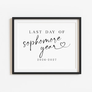 May include: A black framed sign featuring the text LAST DAY OF sophomore year in a mix of serif and script fonts, with a small heart icon at the end of the word year and the numerical date 2026-2027 printed in black on a white background.