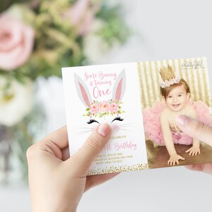 May include: A pink and white bunny rabbit with a floral crown and eyelashes. The text "Some Bunny is turning One" is on the invitation. The invitation has a gold glitter background. A photo of a baby girl wearing a pink tutu and a gold crown is on the right side of the invitation.