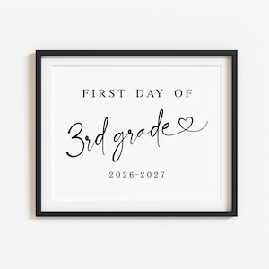 May include: A black rectangular frame containing a white sign with black text that reads FIRST DAY OF 3rd grade with a small heart symbol at the end of the word grade and the school year 2026-2027 printed in black at the bottom.