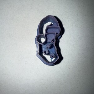 May include: A purple plastic cookie cutter shaped like a cartoon elf with a hat and a beard. The cutter has a hole in the hat and a few holes in the beard.