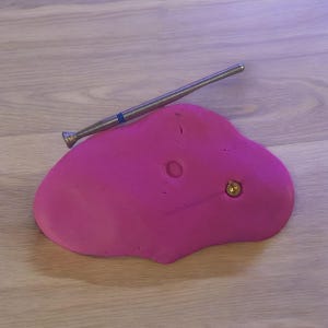 May include: A pink climbing hold with a gold screw and a silver and blue diamond-shaped drill bit.
