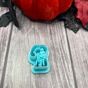 May include: A light blue plastic cookie cutter shaped like a cartoon dog. The dog is sitting with its head tilted to the side and its tongue sticking out.
