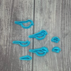 May include: A set of seven blue plastic cookie cutters shaped like birds. The cutters are arranged on a woodgrain surface.