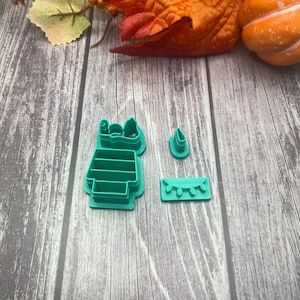 May include: A set of three green plastic cookie cutters shaped like a Christmas tree, a star, and a string of lights.