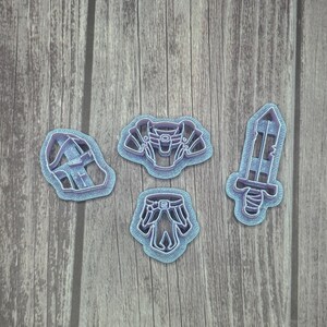 May include: Four blue plastic cookie cutters shaped like a sword, a chest plate, a helmet, and pants.