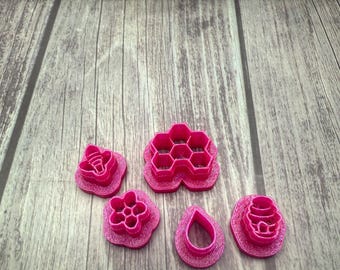 May include: A set of six pink plastic cookie cutters shaped like a bee, honeycomb, flower, teardrop, and two different beehives.